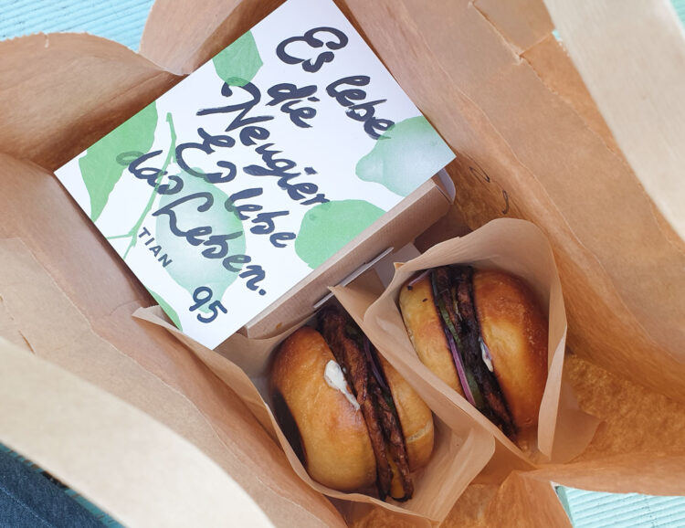 Zwei vegane Burger und Tian-Bistro-Postkarte in einem Papiersackerl