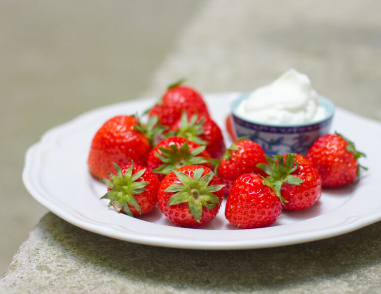Ein Teller Erdbeeren mit einem kleinen Schüsselchen Schlagsahne