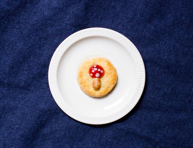 Ein runder Keks mit einer Belegkirsche und einer Mandel, die aussehen wie ein Fliegenpilz
