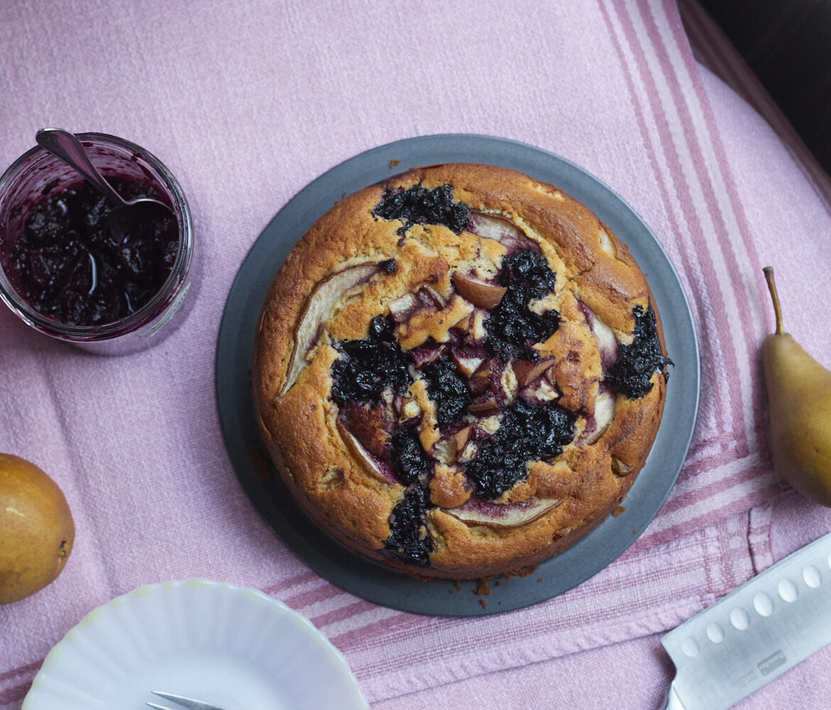 Runder Kuchen, auf der Oberfläche dunkle eingebackene Kleckse aus Apfel-Hollerröster und Birnenstückchen