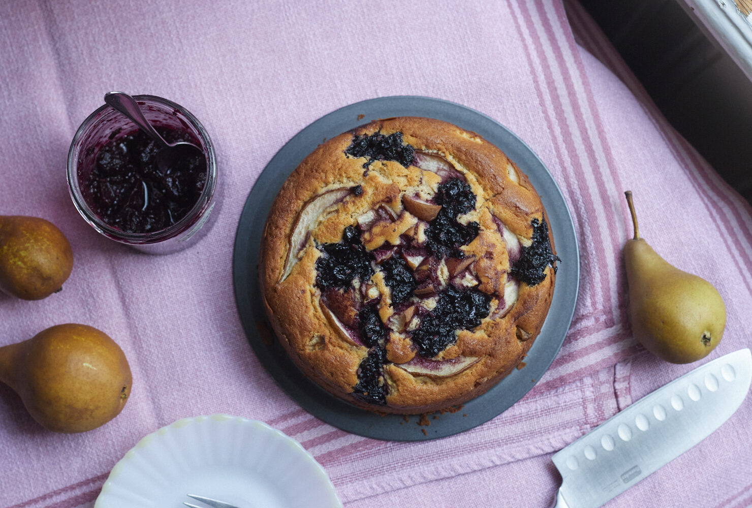 Runder Kuchen, auf der Oberfläche dunkle eingebackene Kleckse aus Apfel-Hollerröster und Birnenstückchen