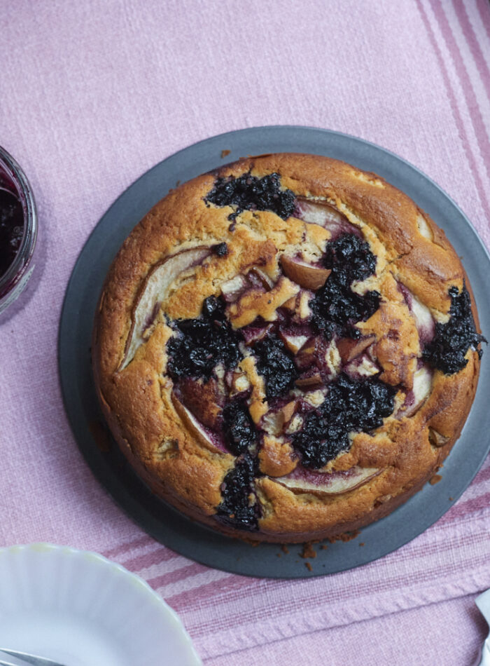 Runder Kuchen, auf der Oberfläche dunkle eingebackene Kleckse aus Apfel-Hollerröster und Birnenstückchen